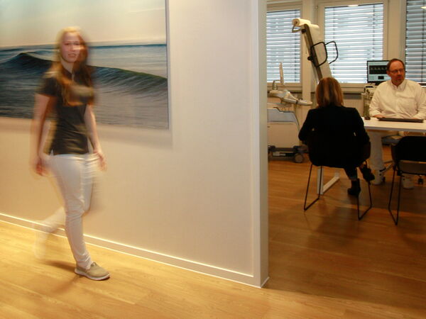 Einblick in den Behandlungsraum, während Mitarbeitende des Praxisteams vorbeigeht.