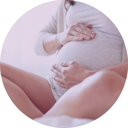 Sitzende schwangere Frau, beide Hände auf dem Babybauch.
