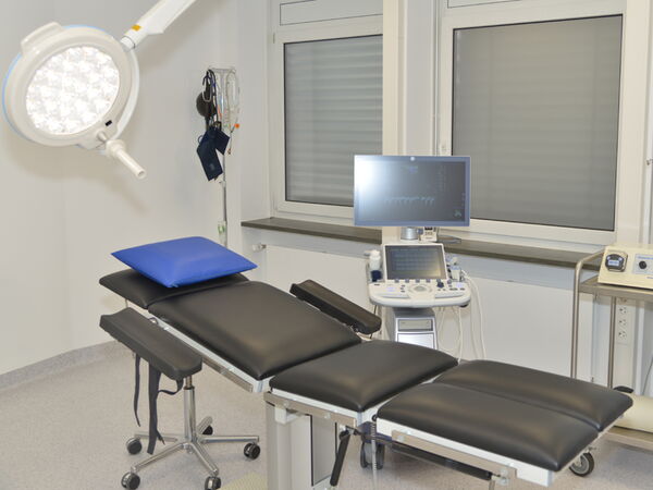 Heller, funktional eingerichteter Operationsraum mit Liege und technischer Ausstattung.